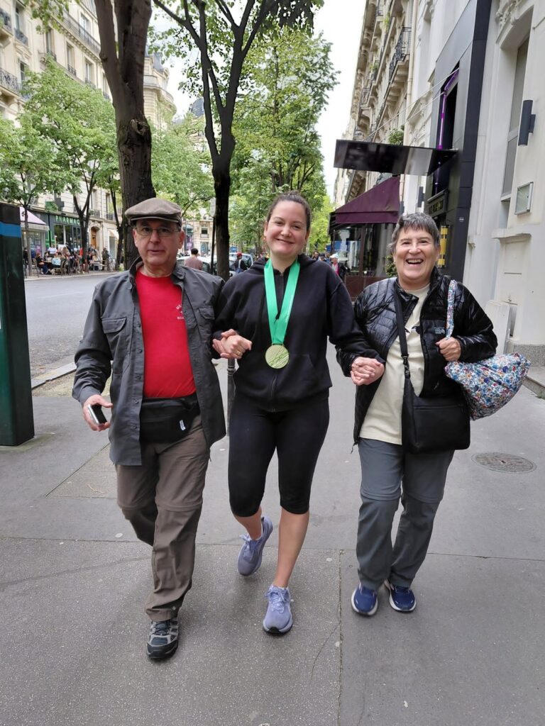Ben and Kathy flanking a woman wearing a Paris Marathon finisher medal on a Paris street