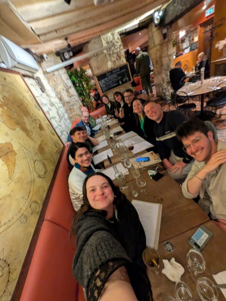 Group of people seated at a long table in a Parisian restaurant with stone walls and a world map