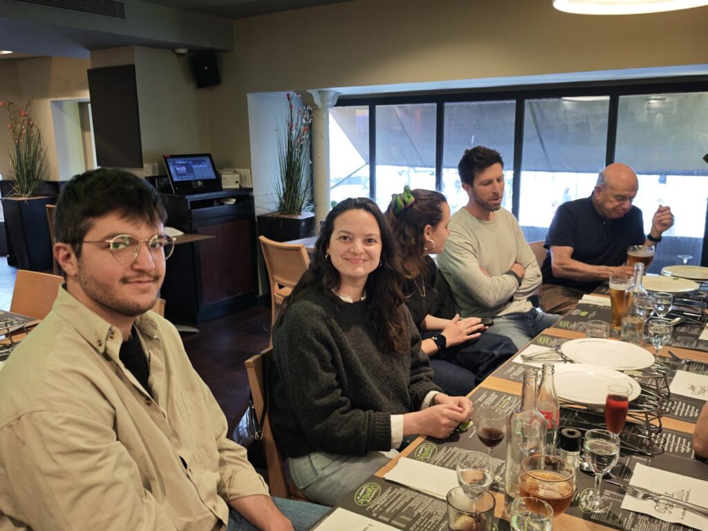 Two people smiling at the camera at a restaurant table, others in the background