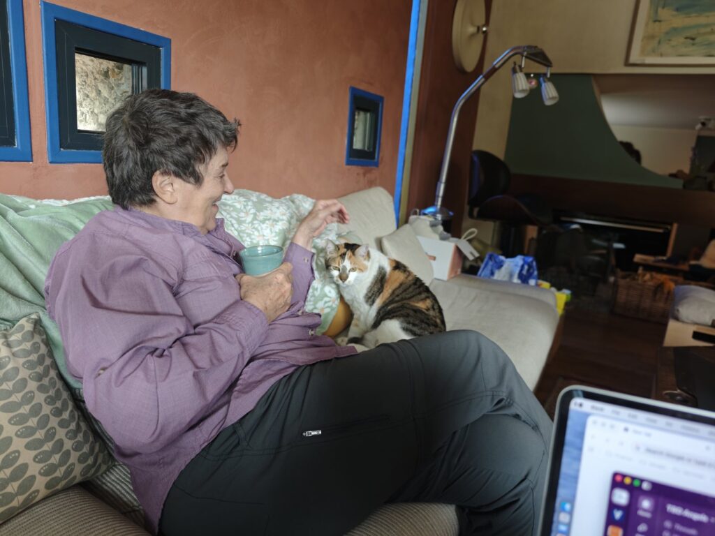 A woman sitting on a couch holding a mug of tea with a calico cat curled up beside her