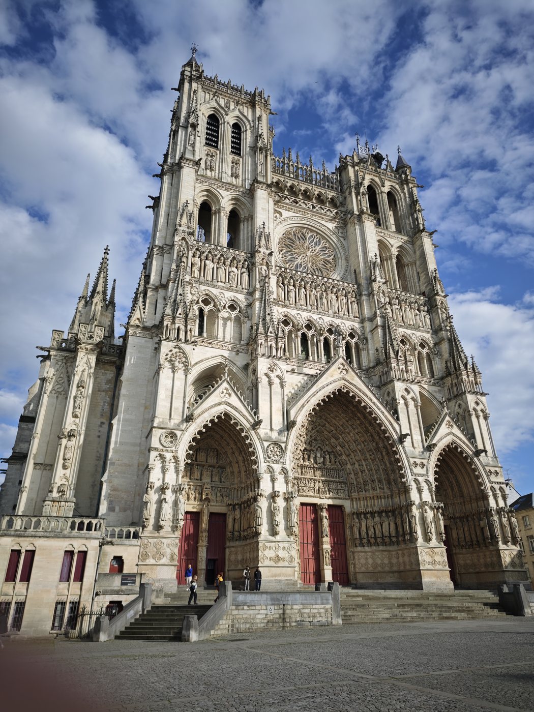 The ornate Gothic facade of Amiens Cathedral under a partly cloudy sky