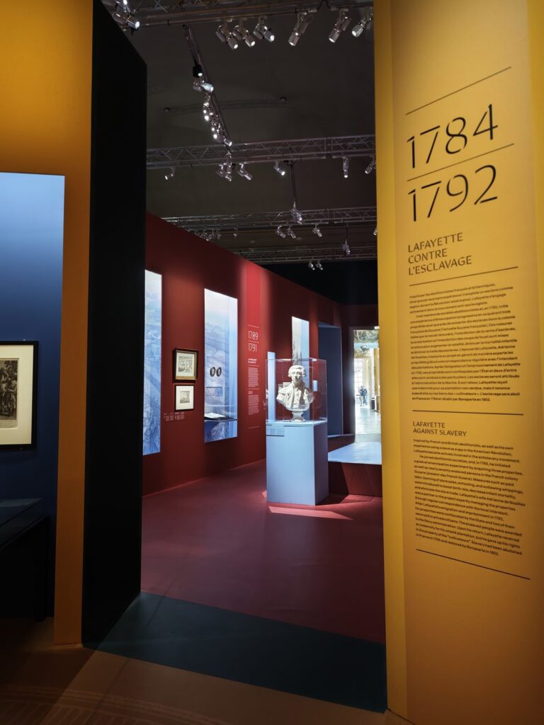 Interior of a museum exhibition about Lafayette and slavery with dramatic red and gold walls and a marble bust