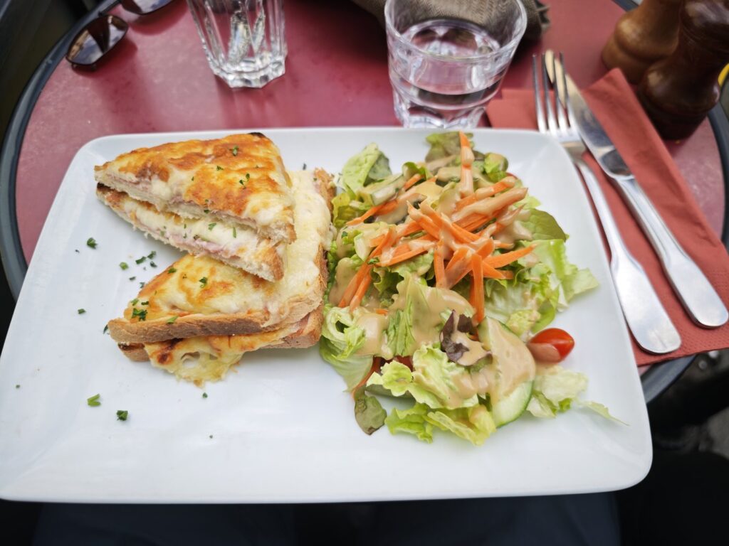 A croque monsieur sandwich with mixed salad on a white plate at a Paris bistro table