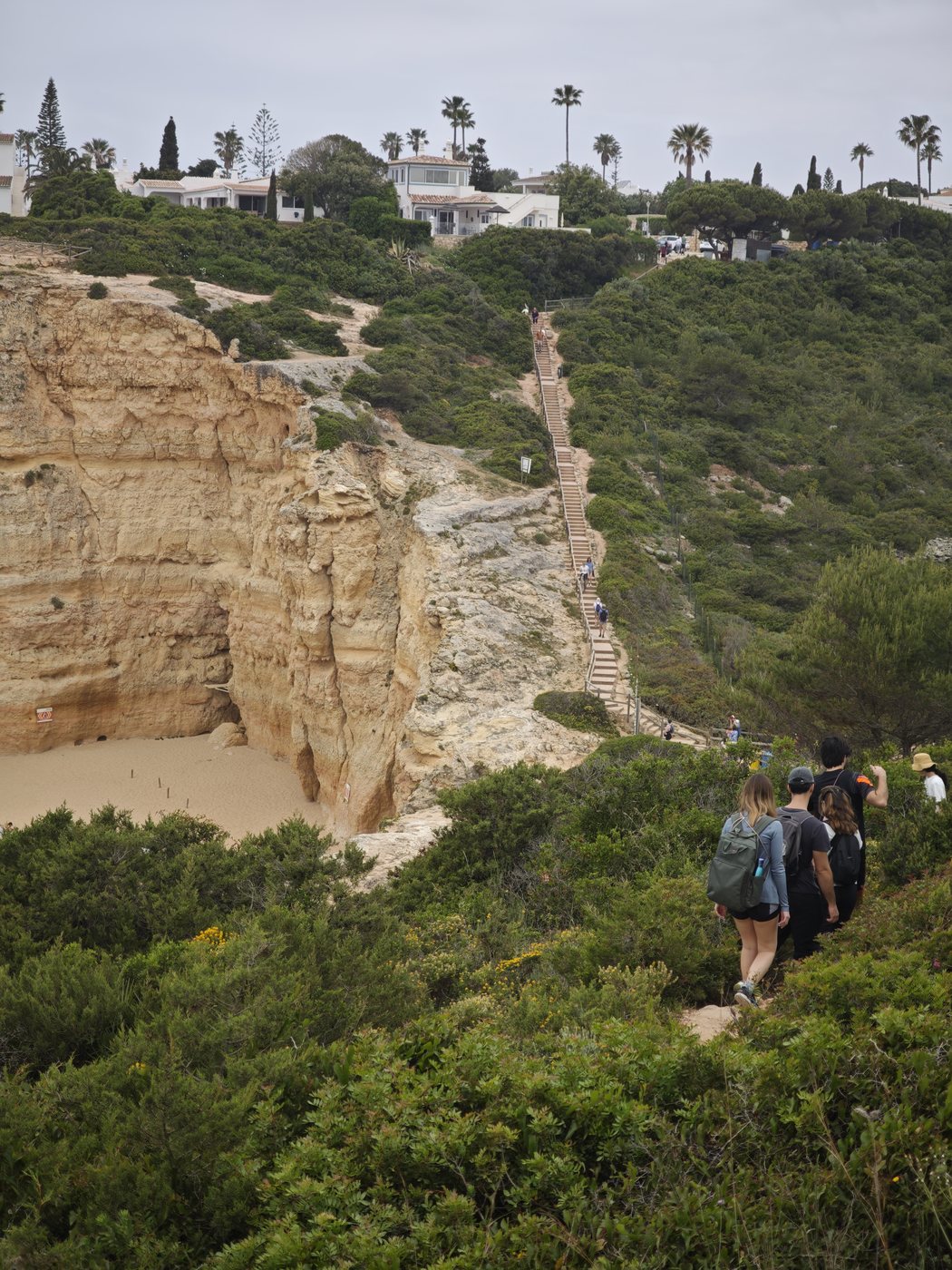 Hikers descending steep cliff stairs toward a beach below