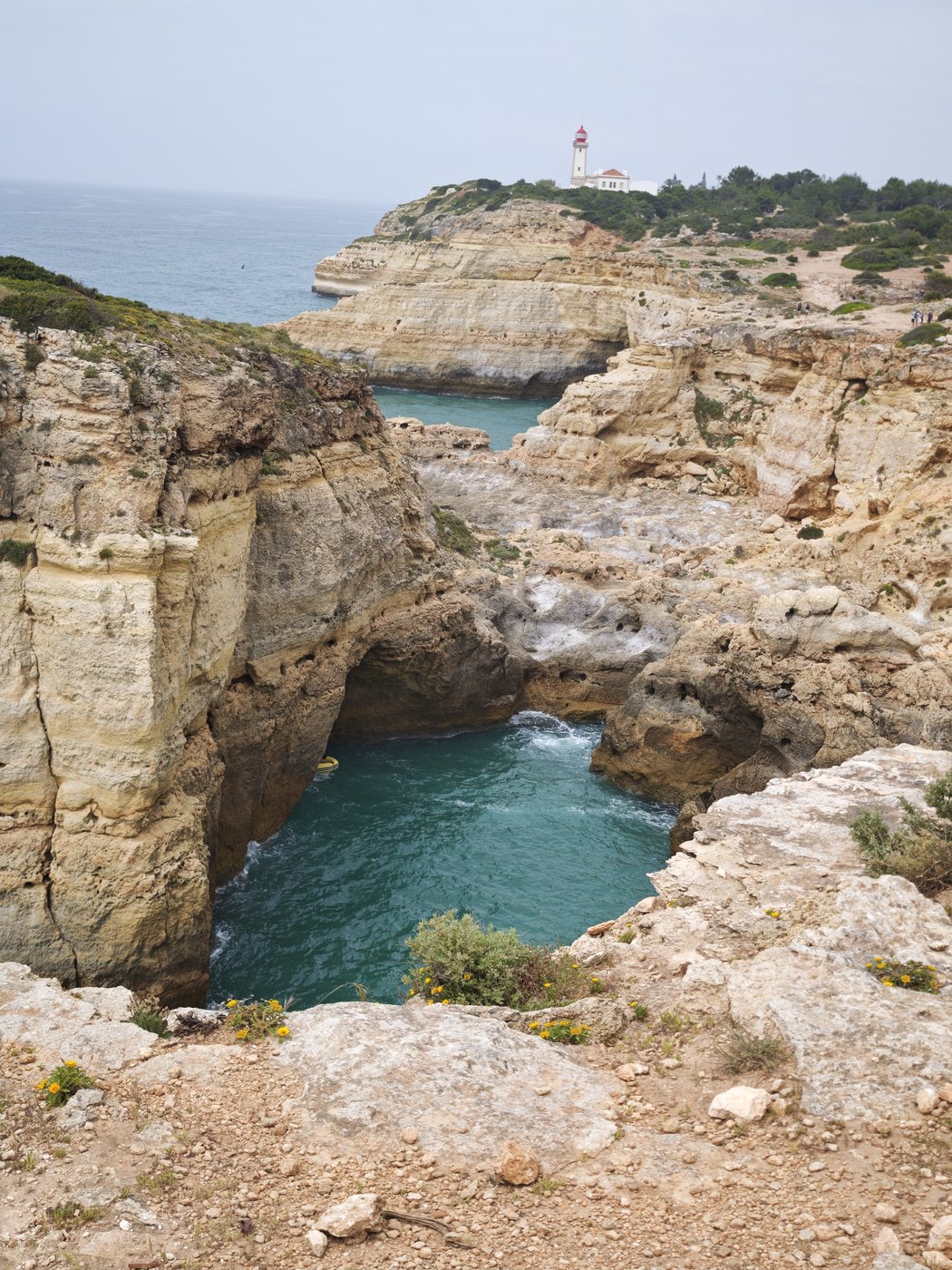 Rock arch over turquoise water with lighthouse in the distance